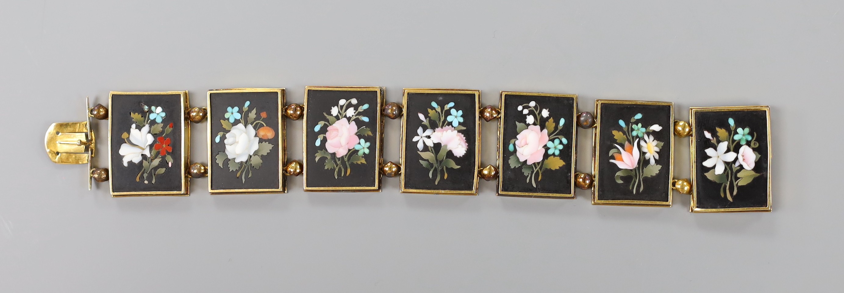 A 19th century Florentine yellow metal bracelet, set with seven pietra dura panels, decorated with flowers, 17cm, gross weight 36 grams.